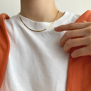 Close-up of minimalist gold flat snake bone chain necklace on a female model