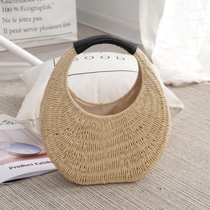 Handmade woven straw tote bag with black leather handle in minimalist home setting