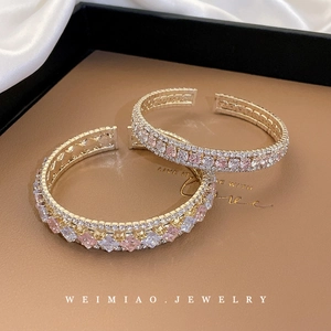Bracelet géométrique doré orné de zircons roses et blancs dans un écrin à bijoux élégant