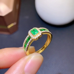 Macro shot of gold emerald-cut green stone ring with side diamonds and vintage details