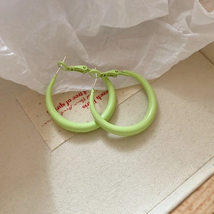 Close-up of bright green hoop earrings on white tissue paper and canvas texture background