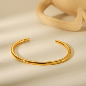 Minimalist 18K gold plated stainless steel open bangle on a natural textured surface