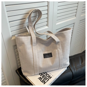 Detailed close-up of oatmeal canvas tote bag on leather sofa with vintage fashion label