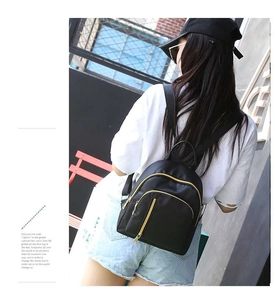 Detail of a black mini waterproof backpack with gold zippers shown in a street lifestyle shot