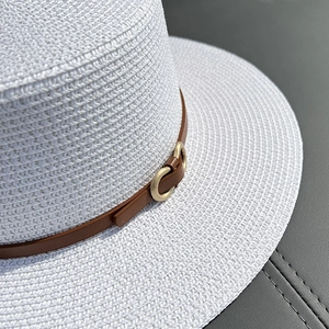 White flat top straw boater hat with a brown leather band and gold metal buckle