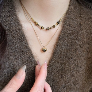Detail of layered tiger eye beaded necklace with a golden heart pendant on a sweater