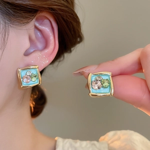 Detail of square gold earrings with pink and green stones in Monet oil painting style
