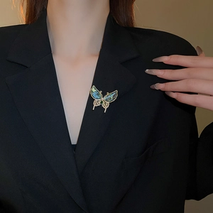 Détail d'une broche papillon avec ailes en nacre portée sur un blazer noir chic