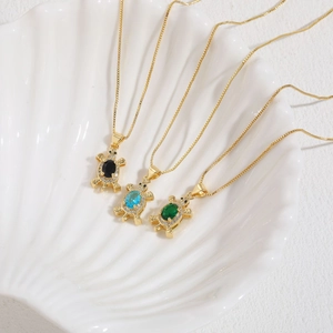 Colliers tortue en or avec pierres de zircon colorées dans un bol en coquillage
