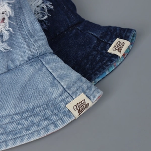 Close-up of denim bucket hat featuring distressed ripped edges and brand woven label