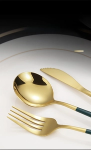 Detailed macro of green and gold stainless steel cutlery set on white ceramic plate