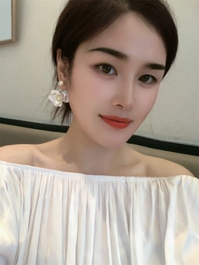 Close-up of white camellia flower earrings with zircon studs on model for elegant look