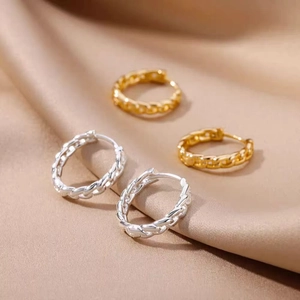 Close-up of gold and silver Cuban link hoop earrings on champagne silk fabric background
