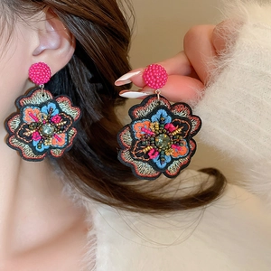 Detailed close-up of embroidered floral earrings with pink beads and colorful ethnic patterns