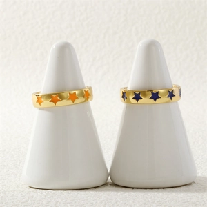 Detail view of gold open rings with orange and blue enamel stars on white stands