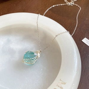 Detailed close-up of blue-green raw stone pendant with gold wire wrap on white marble bowl