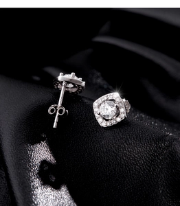 Macro shot of silver square halo stud earrings with brilliant stones on black leather