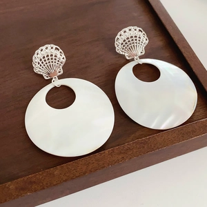 Close-up of starfish shell earrings with large pearlescent round pendants on wood