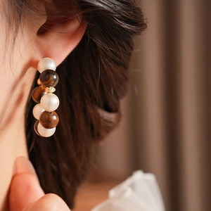 Primer plano de pendientes en forma de C con ojo de tigre y perlas en una modelo