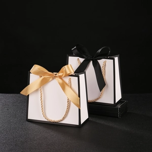Detail of white gift bags with black edges and decorative gold or black ribbon bows