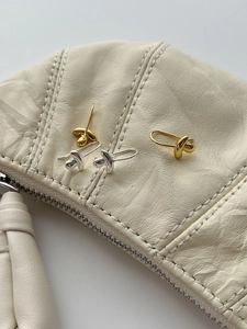 Detail of twisted knot stud earrings in gold and silver finish on textured leather