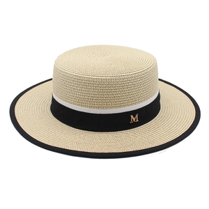 Close-up of beige boater hat with black and white ribbon and gold metal M letter