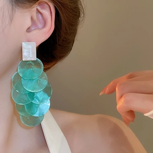 Close-up of long mint green cascading round disc tassel earrings worn by a model