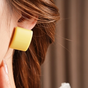 Primo piano di una modella con un orecchino quadrato giallo in resina dal design moderno