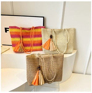 Three straw woven tote bags with colorful stripes and tassels on white display stand