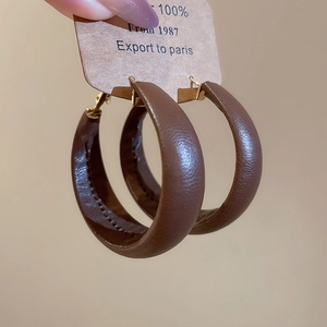 Detail of dark brown leather hoop earrings with golden metal pin and visible stitching