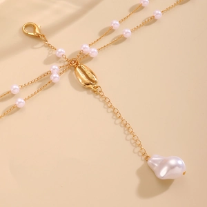 Close-up of golden conch shell pendant with baroque pearl on a body chain