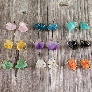 Macro display of nine natural raw stone stud earrings with gold claw settings on wood
