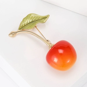 Macro detail of cherry brooch with glossy red fruit and golden leaves on display