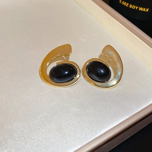 Detailed close-up of golden geometric oval earrings with black stones on textured fabric