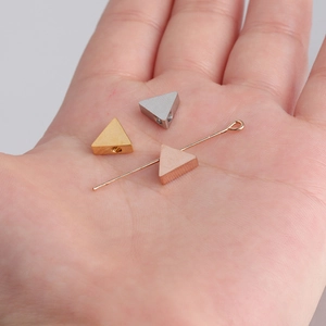 Polished stainless steel triangle beads in gold, silver and rose gold shown on palm