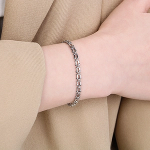 Close-up of a silver U-link chain bracelet on a wrist with a khaki blazer sleeve