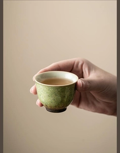 Close-up of hand holding a speckled green ceramic tea cup with a smooth beige interior