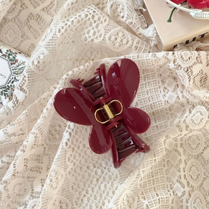 Détail d'une pince à cheveux papillon rouge foncé avec ressort doré sur fond de dentelle