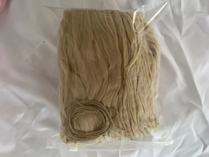 Beige cheesecloth table runner folded in plastic packaging with a small twine roll