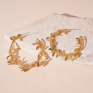 Detail of gold hoop earrings with leaf pendants on light textured stone background