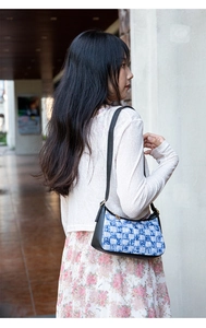Detail of blue and white checkered denim underarm bag with black leather trim and gold zipper