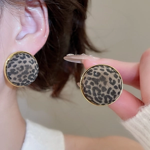Detail of round leopard print earrings with gold metal frame worn by a female model