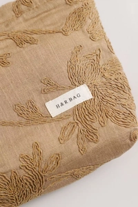 Detail of floral embroidery on beige linen cosmetic bag with a small woven label