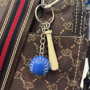 Close-up of blue leather baseball and wooden bat keychain on a patterned bag