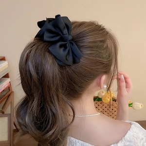 Detail of elegant black satin bow hair clip styled on a half-up ponytail back view