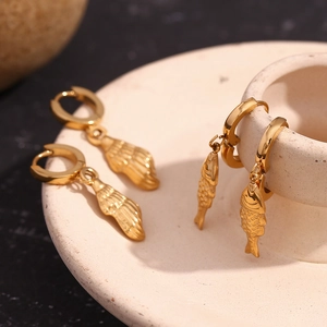Macro shot of gold-plated stainless steel shell and fish pendants on a ceramic tray