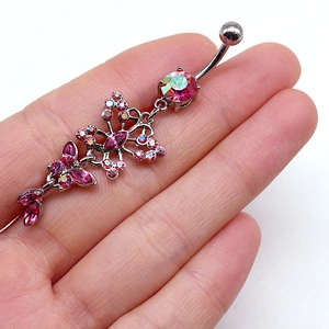 Détail macro du piercing de nombril en argent avec papillon et zircons roses