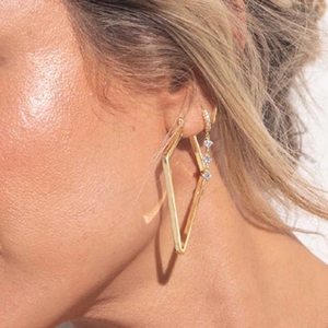 Detailed view of gold rhombic hoop and three-stone drop earring on model's ear