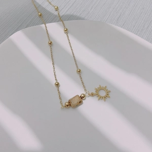 Gold stainless steel sun pendant necklace with natural stone on a white ceramic plate
