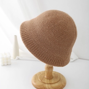 Macro detail of thick caramel knit bucket hat texture on minimalist wood stand